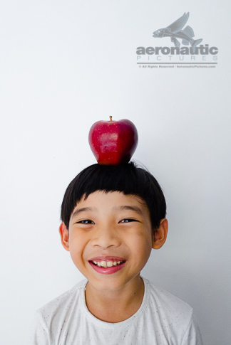 Food Stock Photo - A Happy Kid Smiling Widely with an Apple on His Head Royalty Free Download
